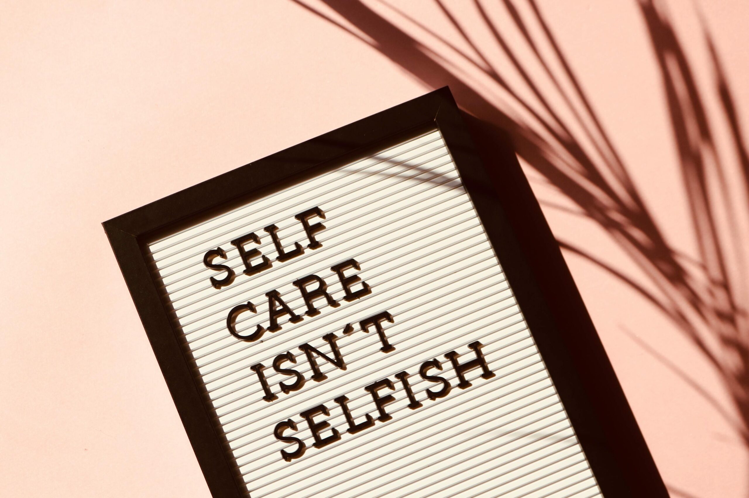 About Letter board displaying 'Self Care Isn't Selfish' with artistic shadow on pink background.